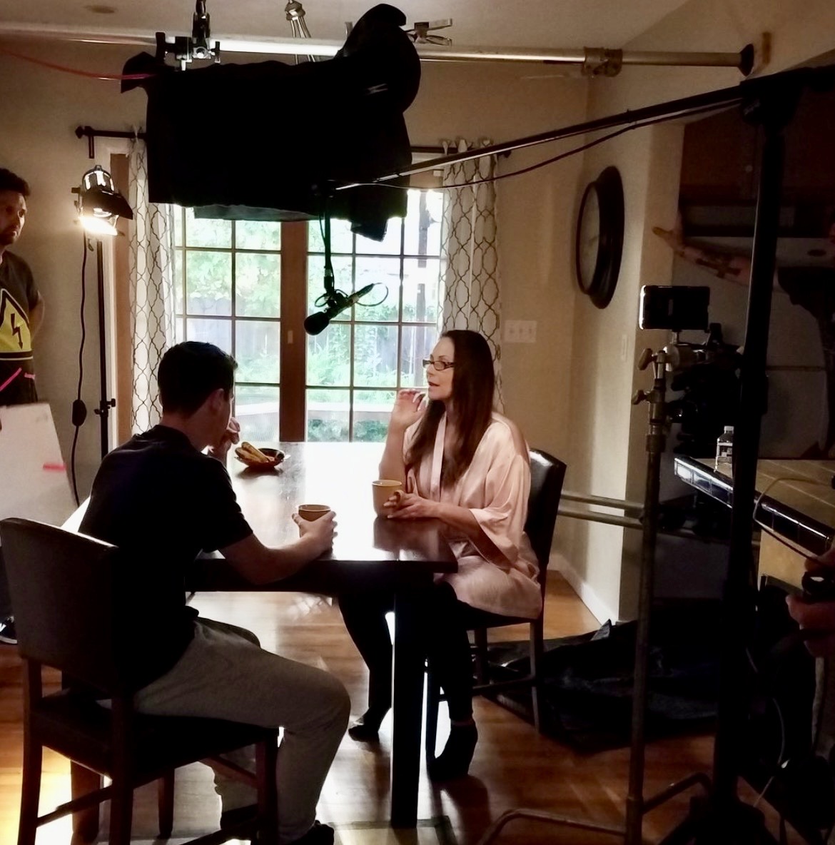 Marie Finch performing at a table on set with the camera, lighting, and boom microphone visible