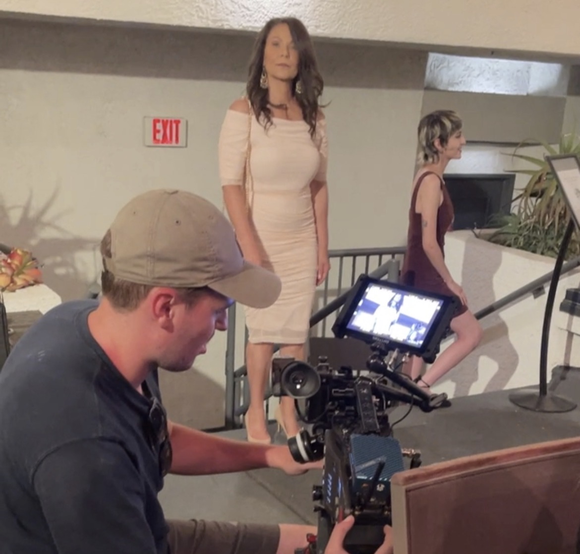 Marie Finch poised in a pale pink dress beside a production camera